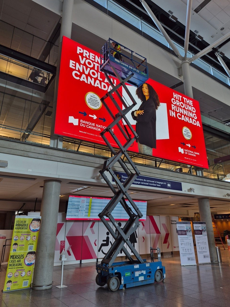 Intervention par plateforme élévatrice devant l’affichage Banque Nationale à l’aéroport Montréal-Trudeau